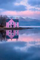 Reflections of a pastel pink house by a tranquil lake with mountains in the background at sunset photo