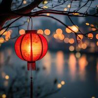 Red lantern illuminating riverside at dusk with city lights in background photo