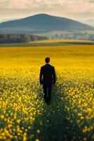 Man walking through vibrant yellow field towards distant hills during sunset photo