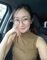 A woman with glasses, wearing a sleeveless beige turtleneck, sits in a car, smiling warmly. photo