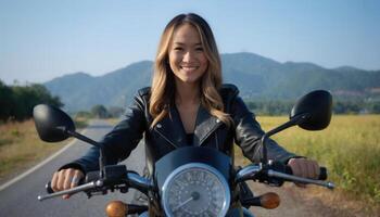 A smiling Asian woman in a leather jacket rides a motorcycle on a scenic mountain road with lush greenery. photo