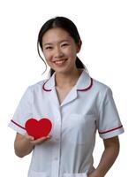 A smiling Asian woman in a white nurse outfit holds a red heart, standing against a plain white background. photo