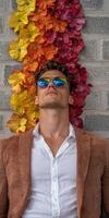 Stylish man in brown corduroy jacket and white shirt posing against a wall of colorful flowers photo