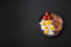 A hearty, delicious breakfast with fried eggs, bacon and tomatoes photo