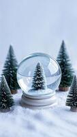Snow globe with Christmas tree inside on white surface, surrounded by miniature Christmas trees photo