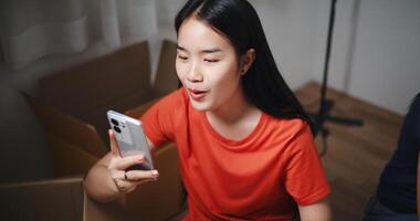 High angle view, Young asian woman sitting on the floor and using mobile phone to check if the items in the boxes they moved from old house are complete. Moving to a new home concept photo