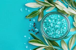 Close-up view of a glass jar filled with blue bath salts surrounded by green leaves and small black peppercorns on a vibrant background photo