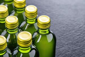 Close-up view of olive-green glass bottles with golden caps resting on a textured dark gray surface showcasing elegant reflections and colors photo