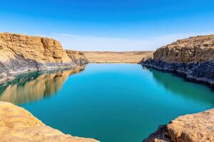 Calm desert oasis featuring teal water reflecting terracotta cliffs and surrounded by black volcanic rocks under a cloudless sky photo
