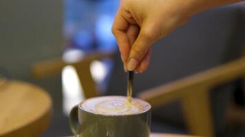 Woman guest stirs creamy coffee with spoon in coffeeshop lit by sunlight closeup. Lady orders caffeine drink with cake at rustic wooden counter. Morning vibes video