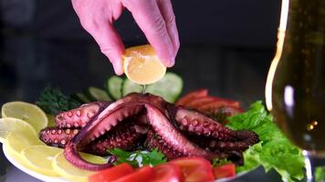 sprinkle octopus with lemon juice Greek tavern restaurant served squid octopus closeup.Hand sprinkling fresh lemon juice on crispy charred octopus tentacles served on a white dish on a tavern table. video