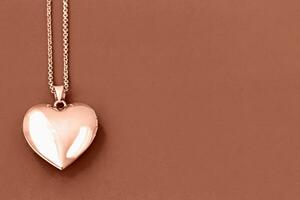 Valentine's Day. Elegant shiny heart-shaped locket on delicate chain on Mocha and Mousse, brown background. Demonstrating color of 2025 year photo
