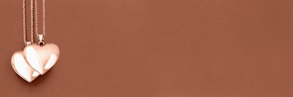 Valentine's Day. Two heart lockets overlapping on Mocha and Mousse, brown background, symbolizing closeness and affection, romance and sentimentality. Banner. Demonstrating color of 2025 year photo