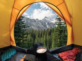 Traveler lying and holding coffee cup in yellow tent and enjoy the view of forest and mountain in national park photo