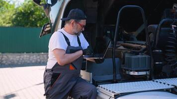 Senior vehicle mechanic with diagnostic tool laptop working near truck in workshop video