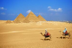 Two people riding camels in front of the pyramids photo