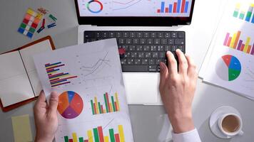 A person is using a laptop with graphs and papers photo