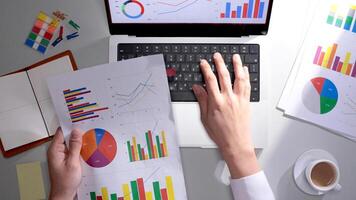 A person is using a laptop with graphs and papers photo