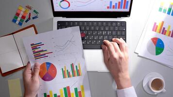 A person is using a laptop with graphs and papers photo