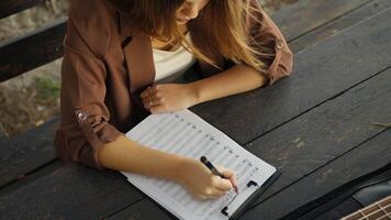Girl Writes Music Notes On Sheet Music Sitting At The Park Table In The Nature video