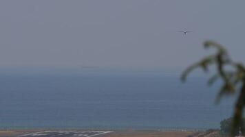 Unknown turboprob airplane approaching landing. Airliner in the sky, long shot. Aeroplane flying. Empty runway and sea. Spotting video