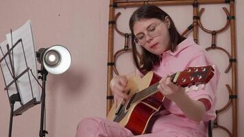 Woman guitarist is performing strumming style of guitar, utilizing six string acoustic instrument. Performance is taking place in musician's home studio in session of practice. Handheld shot, zoom in video