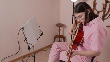 Woman guitarist performs in strumming style characteristic of classical six string acoustic guitars in musician's home studio, engaged in session of practice. High angle view, handheld shot, zoom in video