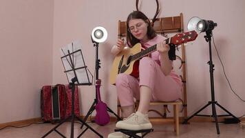 Woman plays classical guitar energetically performs in home studio, utilizing strumming technique. She engaged in process of practicing, music education with facial expression. Handheld, zoom in video