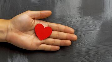Human hand holds red paper heart against textured gray closeup image. Minimalistic composition close up photography. Love, kindness and human connection concept photo realistic