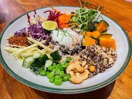 Bowl dish with brown rice, cucumber, tomato, green peas, red cabbage, chickpea, fresh lettuce salad and cashew nuts. Healthy balanced eating photo