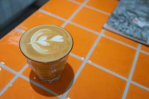 Top view of hot latte coffee with latte art in a glass on orange tile table, copy sapce concept. photo