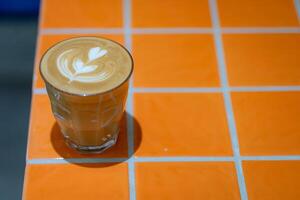 Top view of hot latte coffee with latte art in a glass on orange tile table photo
