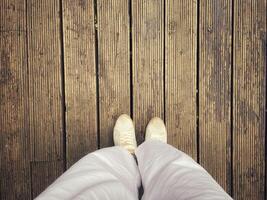 Top of legs in jeans and brown sneakers on wooden table on wooden background in vintage tone and copy space concept. photo