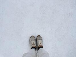 Top of legs in white jeans and brown sneakers on white snow in copy space concept. photo