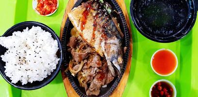 Flat lay or top view Saba and fried onion with teriyaki sauce with white rice and black bowl of soup on the green table at canteen. Delicious and Korean food concept. photo