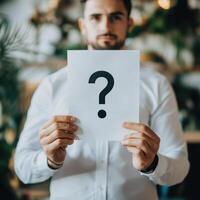 Man holding question mark sign in focus, blurred background photo