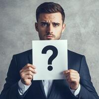 Man holding question mark paper, thoughtful expression, gray background photo