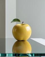 Golden apple with stem and leaf sits on a reflective surface. photo