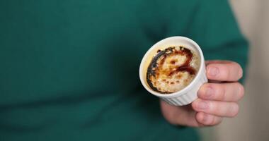 Hand holds a small cup filled with a creamy dessert, topped with a caramelized glaze, in a warm and inviting atmosphere, perfect for enjoying sweet moments. Caramelizing sugar on top of creme brulee video
