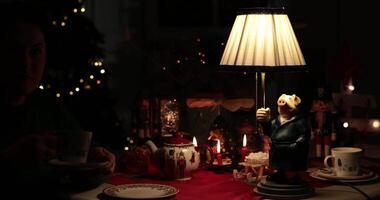 Woman enjoy a warm holiday evening tea time around a beautifully Christmas table setting. The whimsical pig lamp adds charm to the festive atmosphere with ambient lighting. video