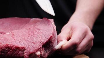 A butcher removes the fascia from a beef steak with a large knife in a dark room video