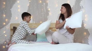 Beautiful girl and little boy with short hair have fun hitting each other by paddles sitting on the bed video