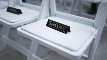 Reserved White Chair at an Elegant Event. A close-up of a white cushioned chair with a Reserved sign in a sophisticated setting. Perfect for wedding, conference, or formal event themes. video