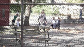 Playground Scene Through Chain-Link Fence. A view of children playing in a sunny playground, seen through a chain-link fence. The blurred background highlights the fence's texture video
