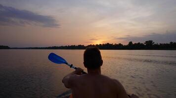 A man kayaks on a calm river towards the sunset. He skillfully rowing oar. Beautiful nature of the evening river. Super Slow Motion video