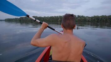 A man kayaks on a calm river. He skillfully rowing oar. Beautiful nature of the evening river. Super Slow Motion video