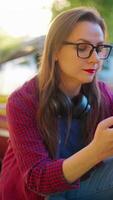 Woman is standing crouched down next the red vintage car and using smartphone video