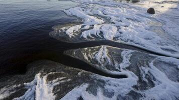 Close-up of the frozen shoreline of Lake Ladoga, showing intricate ice patterns forming along the water's edge. The icy surface contrasts with the dark, calm water under winter light video