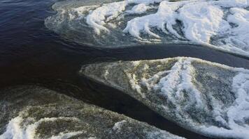 Close-up of the frozen shoreline of Lake Ladoga, showing intricate ice patterns forming along the water's edge. The icy surface contrasts with the dark, calm water under winter light video