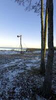 un de cerca de un resistido molino en pie en el Nevado apuntalar de lago ladoga, con calma agua y cañas en el antecedentes. el puesta de sol ligero Destacar el rústico estructura en contra el invierno video